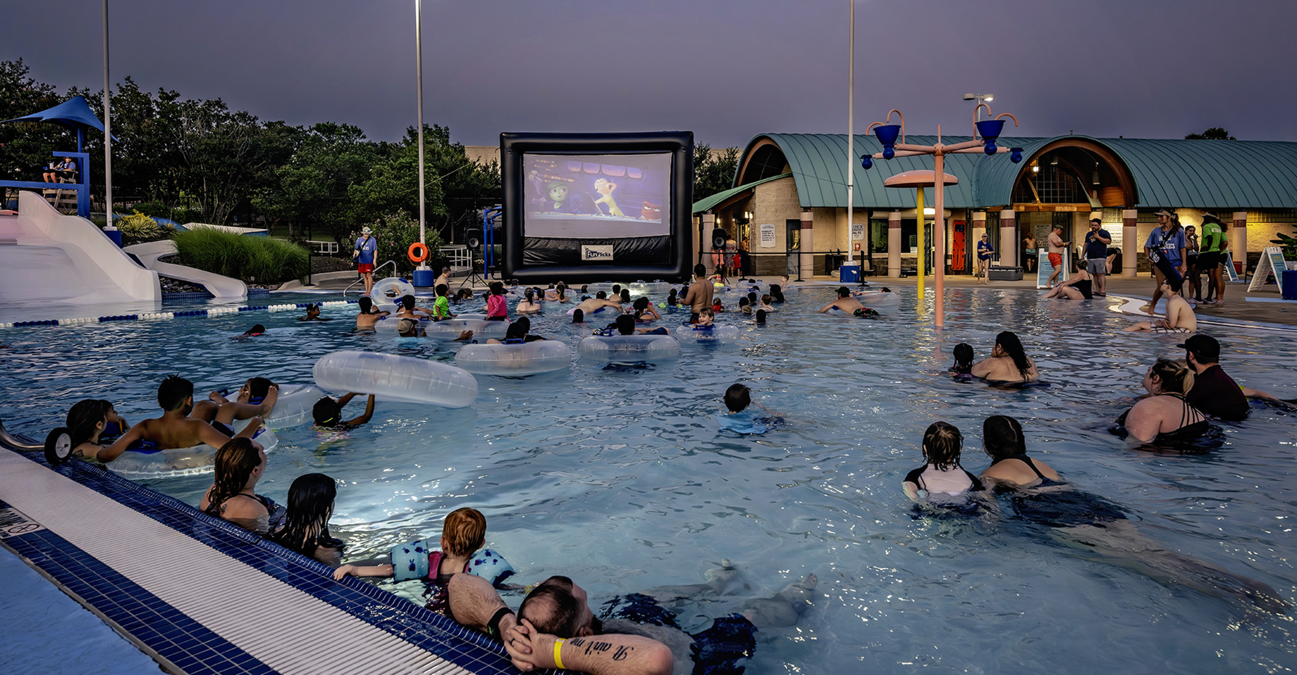 People enjoying the pool while watching a movie on a large screen, creating a cinematic experience in the water.